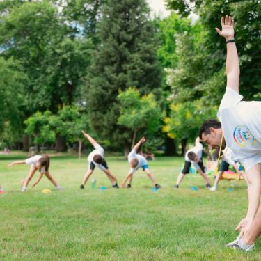 Kids stretching exercises in a park guided by a coach, promoting fitness and fun.